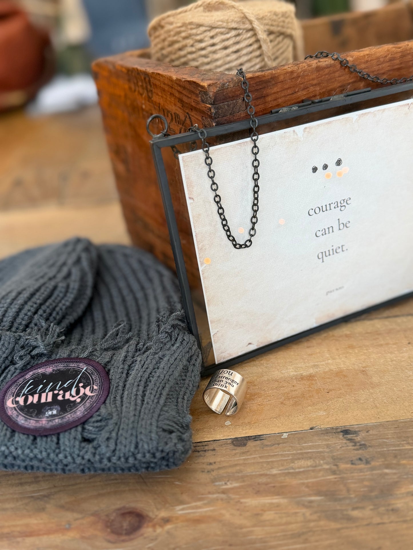 Gray knit beanie with a purple label, necklace, and card on a wooden surface
