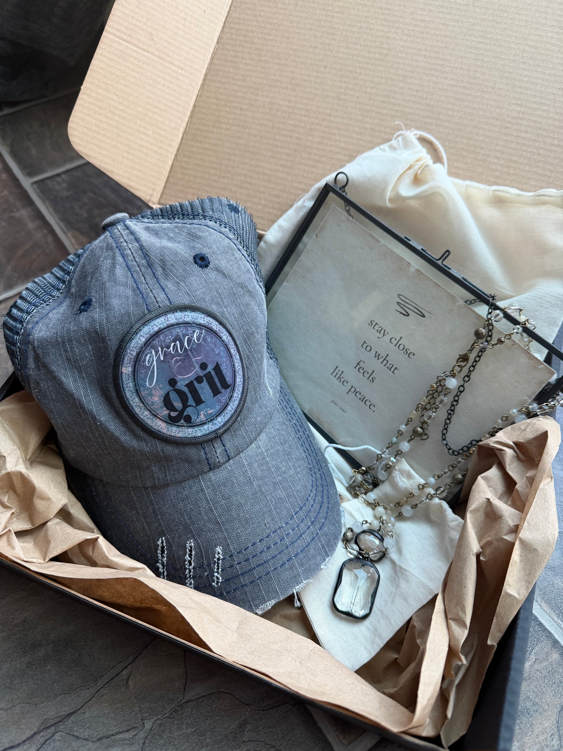 Gray cap with 'grit' logo on a cardboard box with jewelry and a book.