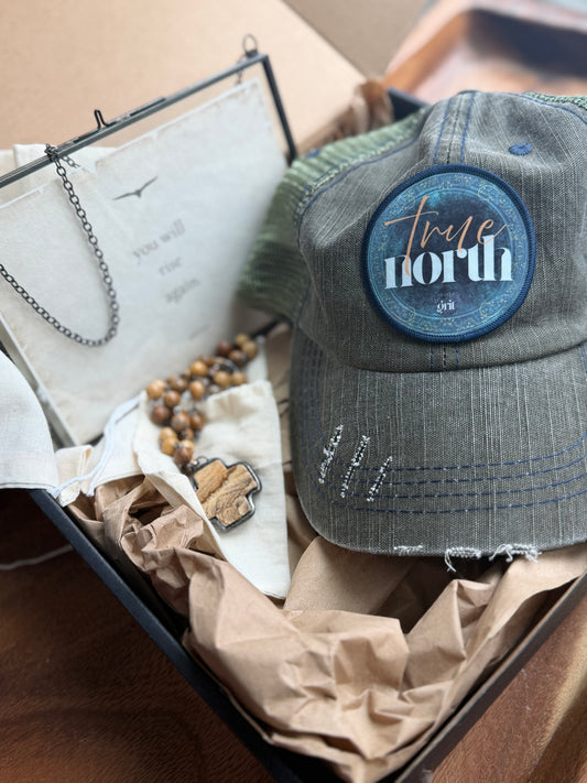 Gray cap with 'True North' patch in a box with other items