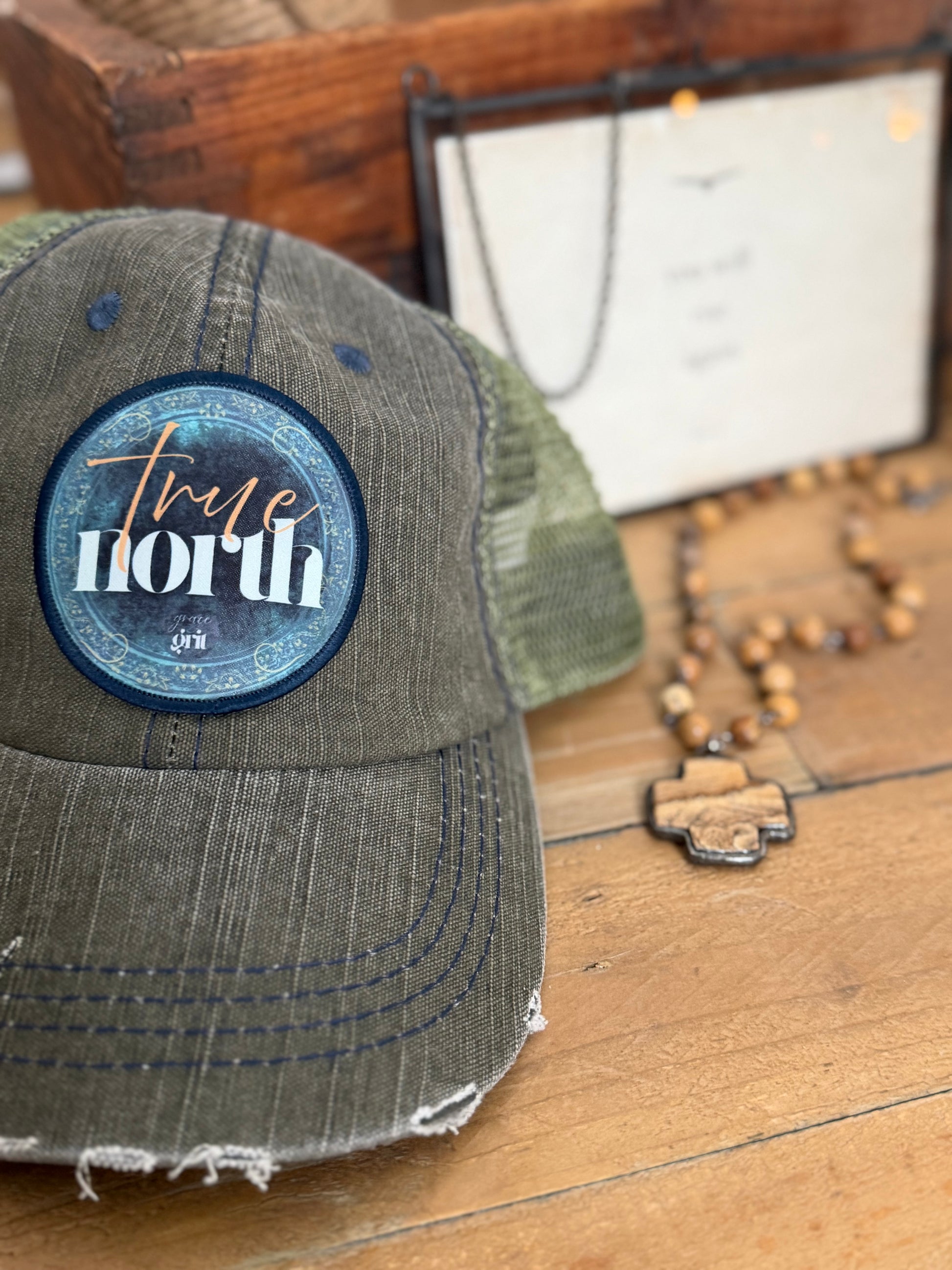 Green cap with 'True North' patch on a wooden surface
