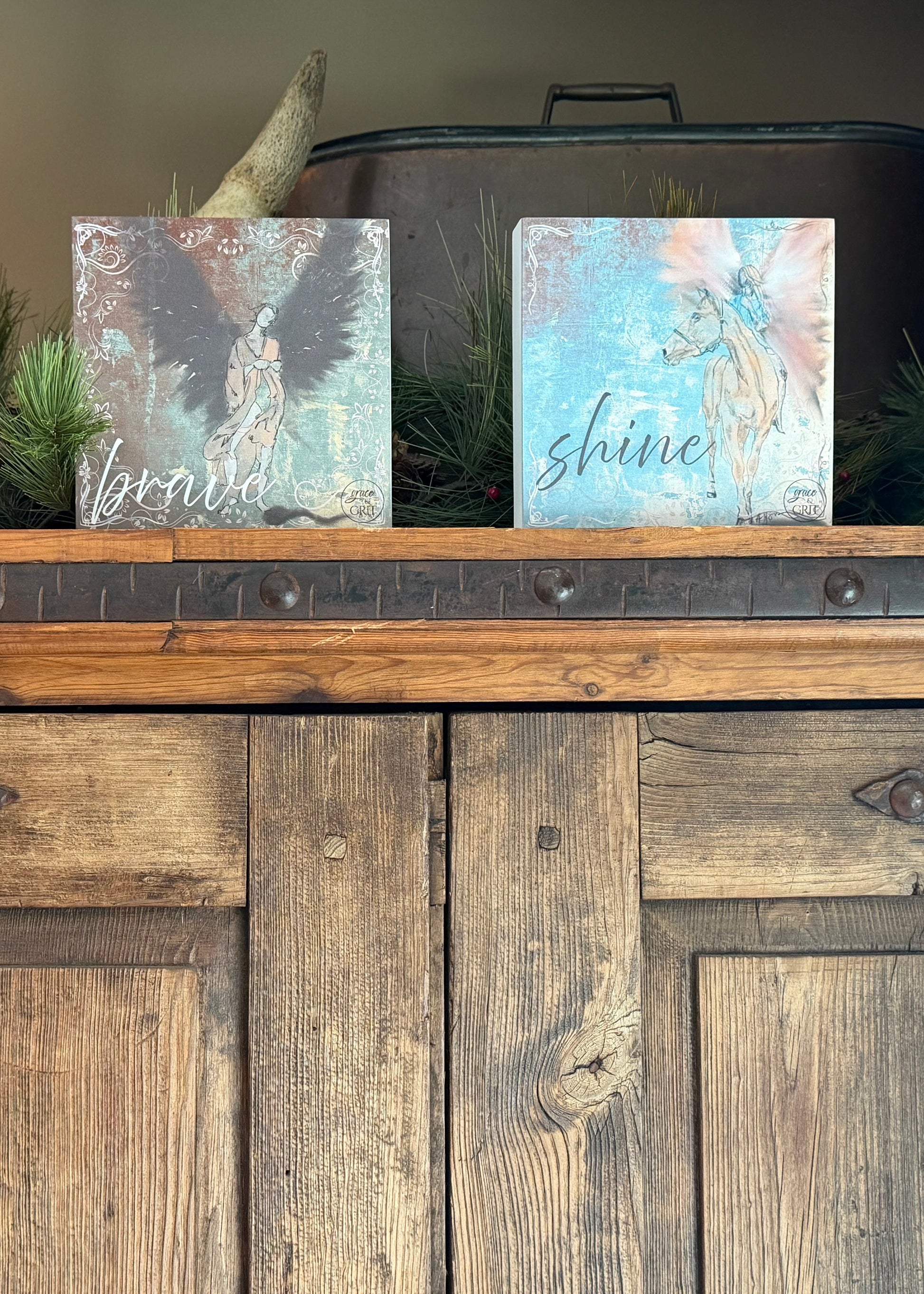 Decorative signs with angel designs and motivational phrases on a wooden surface.