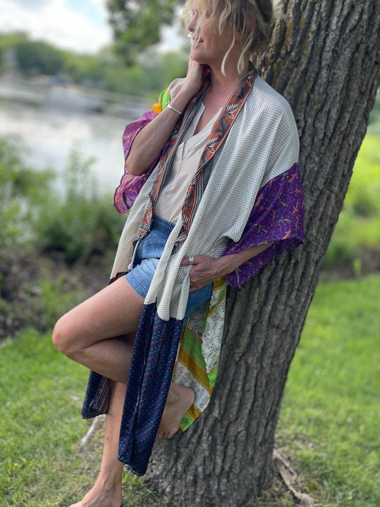 Woman sitting against a tree by a body of water wearing a colorful kimono.