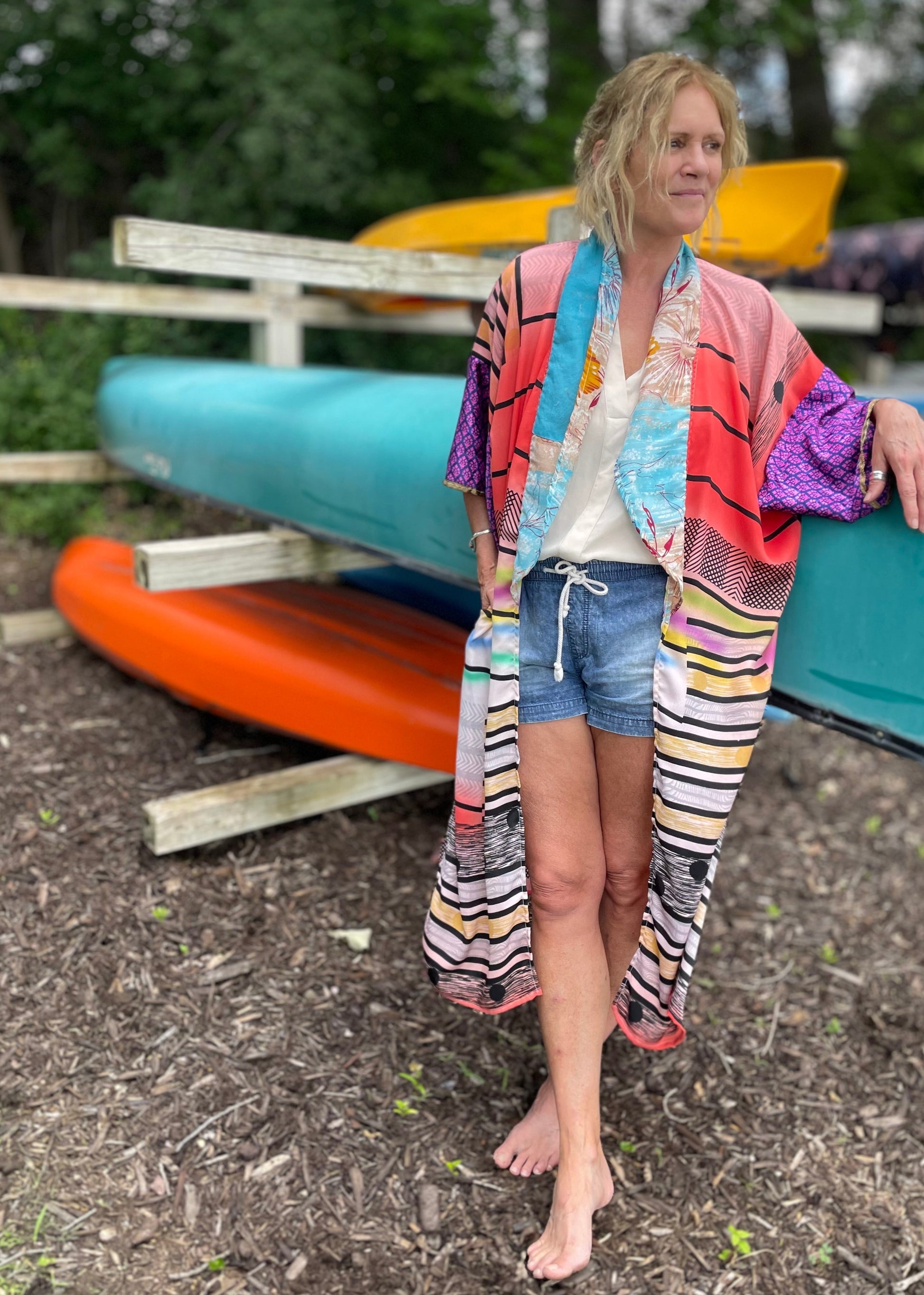 A woman standing outdoors with a colorful silk kimono and kayaks in the background